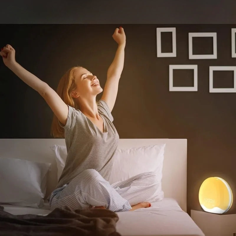 Réveil LED Aube Colorée Double Face posé sur table de chevet, femme s’étirant au réveil grâce à la lumière naturelle.