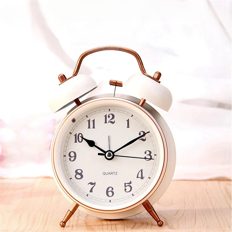 Réveil vintage blanc à double cloche sur fond clair, cadran blanc et aiguilles noires.