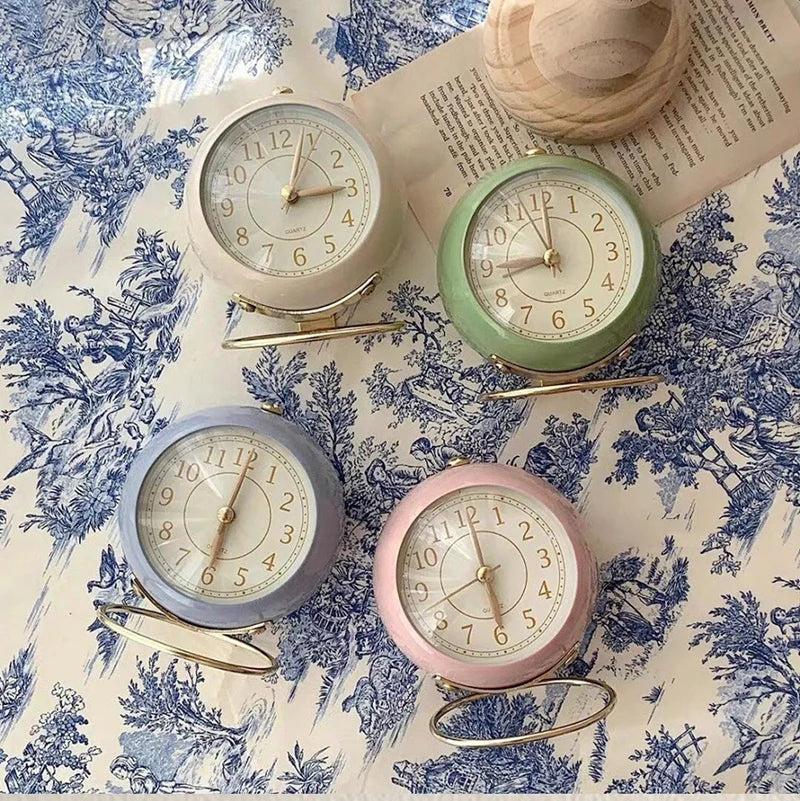 Collection de Réveils Vintage Silencieux Ronds en plusieurs couleurs pastel – vert, rose, gris et beige – disposés sur fond bleu décoratif.