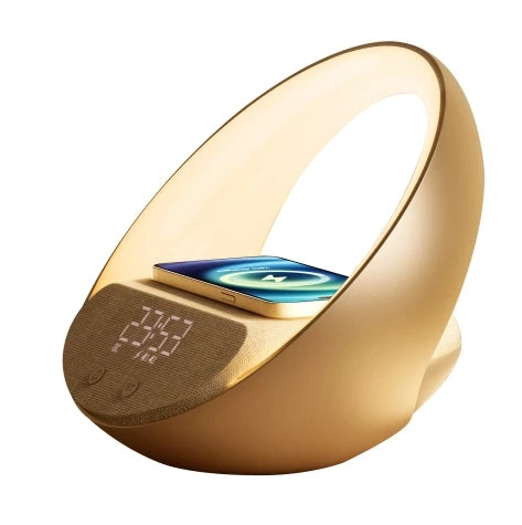 Le Doux Reveils Réveil Connecté 4-en-1 est doté d'une finition dorée, d'un haut-parleur Bluetooth, d'une lampe RGB, d'un socle de recharge sans fil sur le dessus et d'un affichage numérique de l'heure éclairé sur le devant.