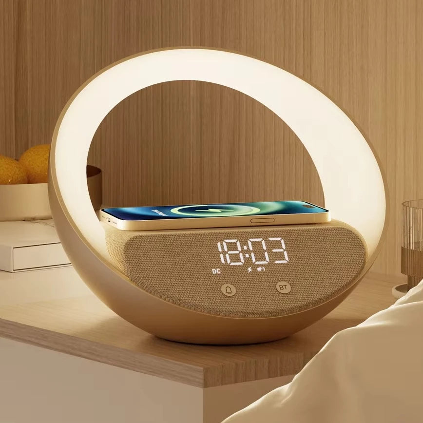 Le Doux Reveils Réveil Connecté 4-en-1 avec haut-parleur Bluetooth, chargeur sans fil, lampe RGB et alarme est posé sur une table de chevet et éclaire doucement la pièce. Un smartphone est posé sur l'horloge à côté d'un bol d'oranges.