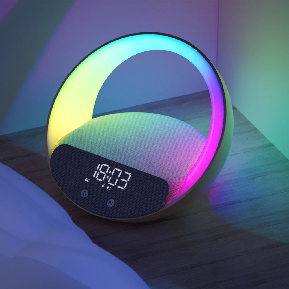 Le Doux Reveils Réveil Connecté 4-en-1 présente un design circulaire, une lampe RGB, un haut-parleur Bluetooth, un système de recharge sans fil et une alarme. Il est posé sur une table de nuit en bois et affiche l'heure 18:03 en chiffres numériques blancs.
