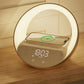 Un Doux Reveils Réveil Connecté 4-en-1 avec écran numérique, haut-parleur Bluetooth, lampe RGB et chargeur sans fil est posé sur du bois. Un smartphone se recharge sans fil sur le dessus, indiqué par une icône, tandis que l'anneau LED de l'horloge ajoute une touche de modernité.