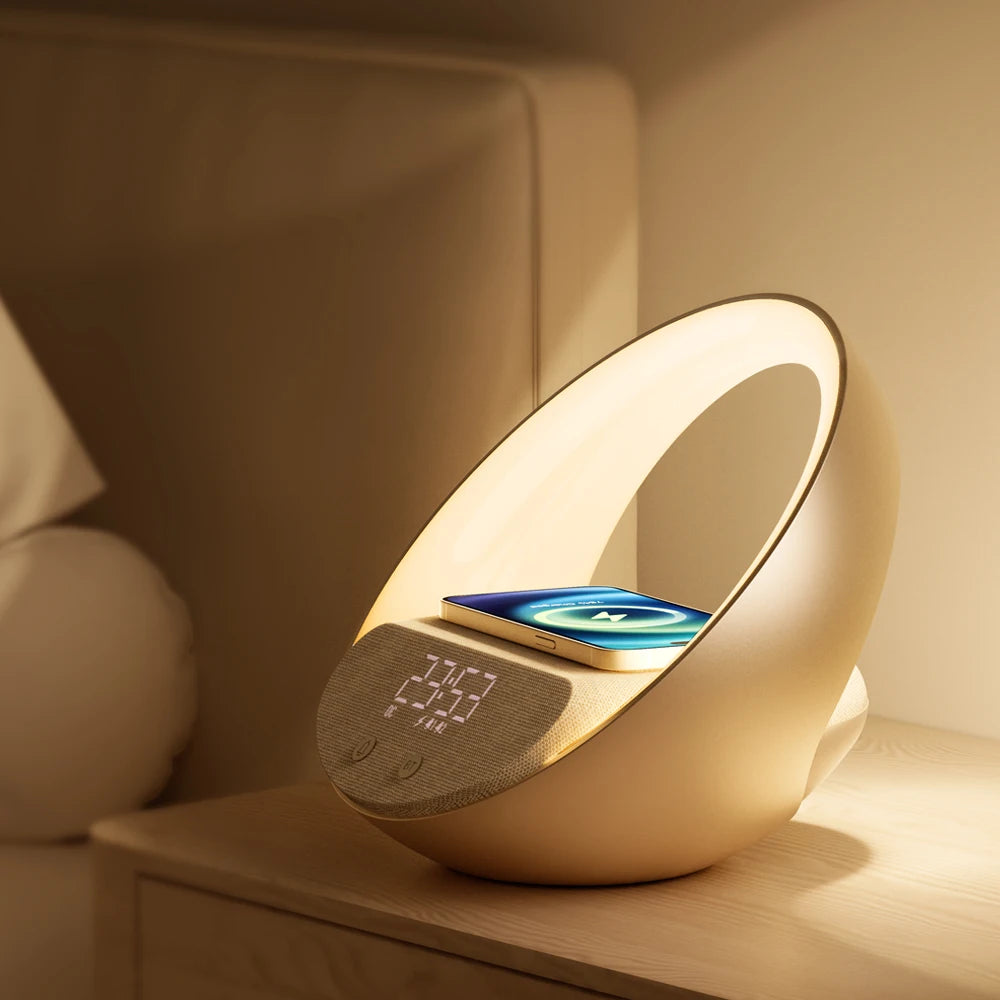 The Doux Reveils Réveil Connecté 4-en-1 avec enceinte Bluetooth, chargeur sans fil, lampe RGB et alarme trône sur une table de nuit en bois, près d'un lit.