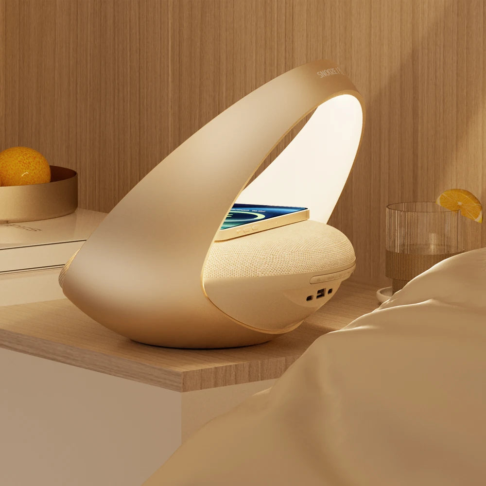 La Doux Reveils Réveil Connecté 4-en-1 - une lampe de chevet ovale avec éclairage RVB, haut-parleur Bluetooth, alarme et recharge sans fil - accueille votre téléphone sur une table de nuit près d'un lit, à côté d'un verre d'eau citronnée et d'un bol d'oranges.