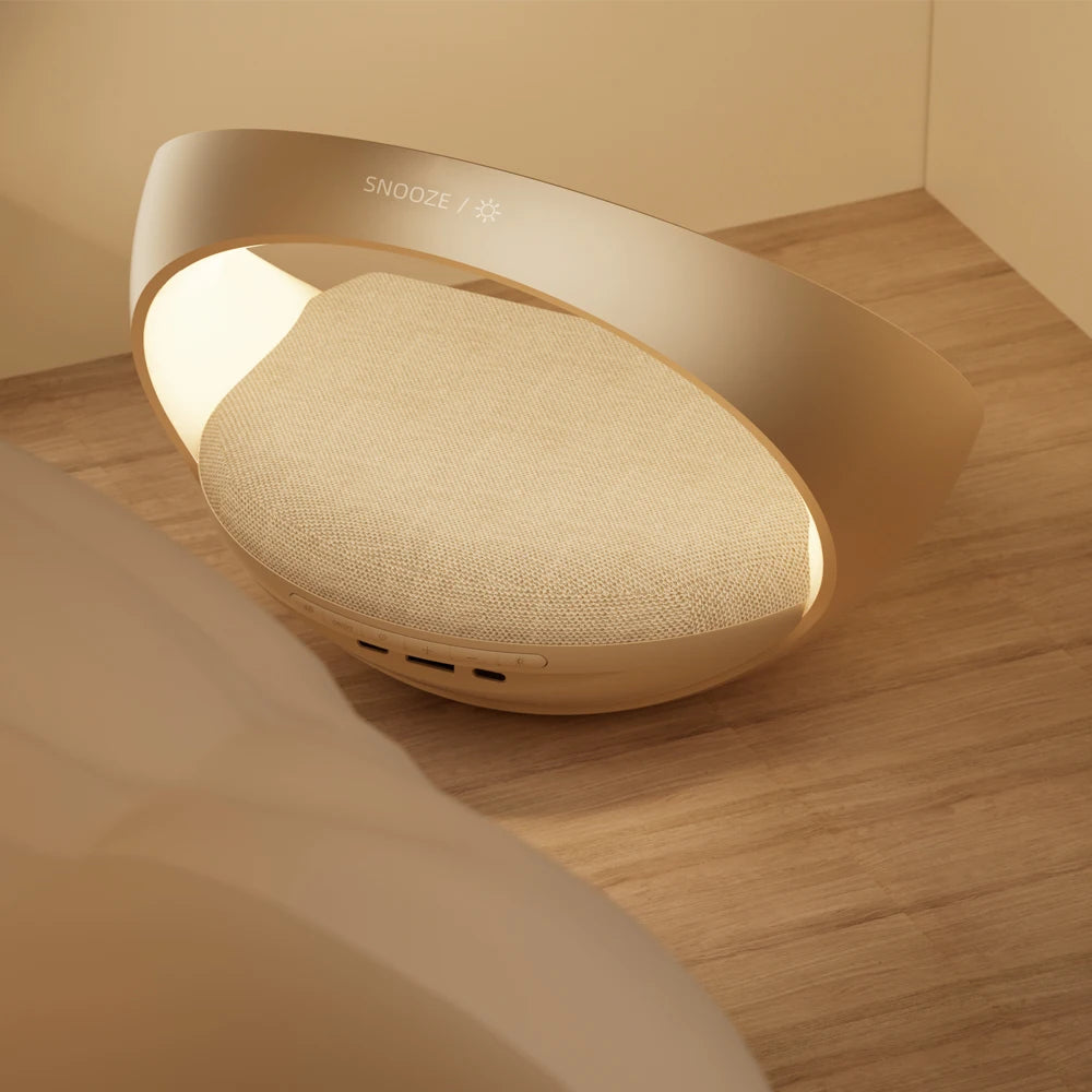 Le Doux Reveils Réveil Connecté 4-en-1 combine une lampe RVB, un haut-parleur Bluetooth, un chargeur sans fil et une alarme. Son design ovale moderne comprend un coussin en tissu et un bouton SNOOZE - parfait à côté de votre lit pour le confort et le style.