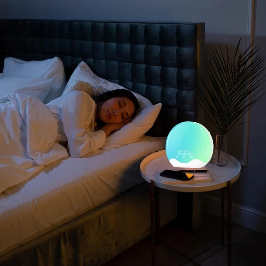 Réveil LED Aube Colorée sur table de chevet, femme dormant paisiblement sous lumière turquoise.