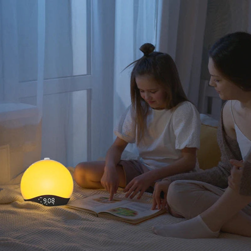 Réveil Simulateur d’Aube – Lever et Coucher de Soleil allumé sur table de chevet, mère et fille lisant ensemble.