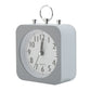 Réveil carré gris au design moderne vu de côté, avec cadran blanc et anneau chromé.