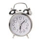 Réveil vintage argenté à double cloche, cadran blanc et chiffres noirs sur fond clair.