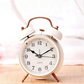 Réveil vintage blanc à double cloche sur fond clair, cadran blanc et aiguilles noires.