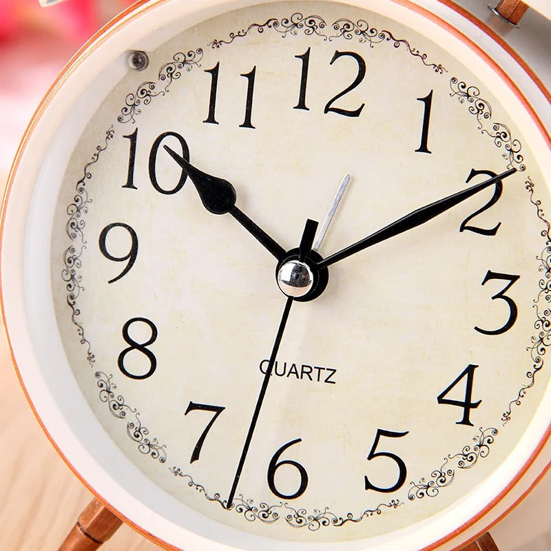 Gros plan du cadran d’un réveil vintage blanc avec aiguilles noires et décorations florales fines.