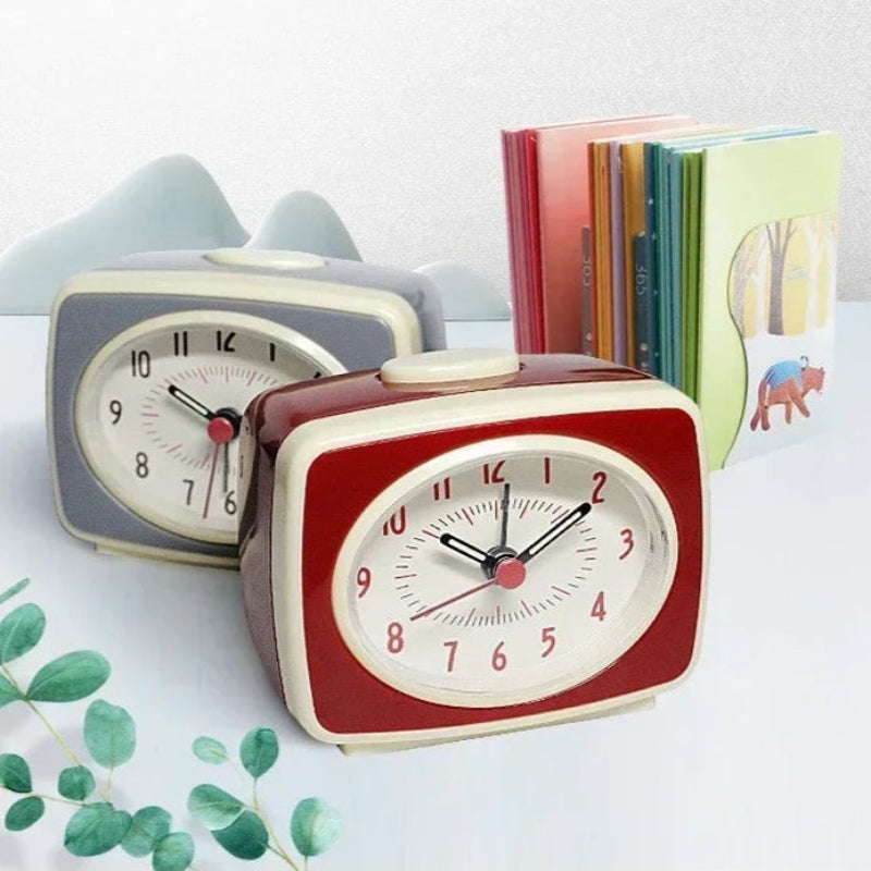 Réveil Vintage Nordique avec Aiguilles Fluorescentes, un de couleur rouge et un autre de couleur grise posé sur une table a coté de livres 