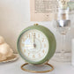 Réveil Vintage Silencieux Rond vert pastel sur table avec bougie et verre décoratif, ambiance douce et élégante.