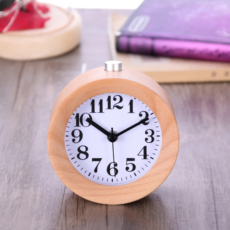 Réveil rond en bois posé sur un bureau, cadran blanc lisible avec livres en arrière-plan.