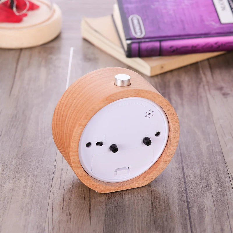 Réveil rond en bois vu de dos, panneau blanc avec commandes et compartiment à piles ouvert sur un bureau.